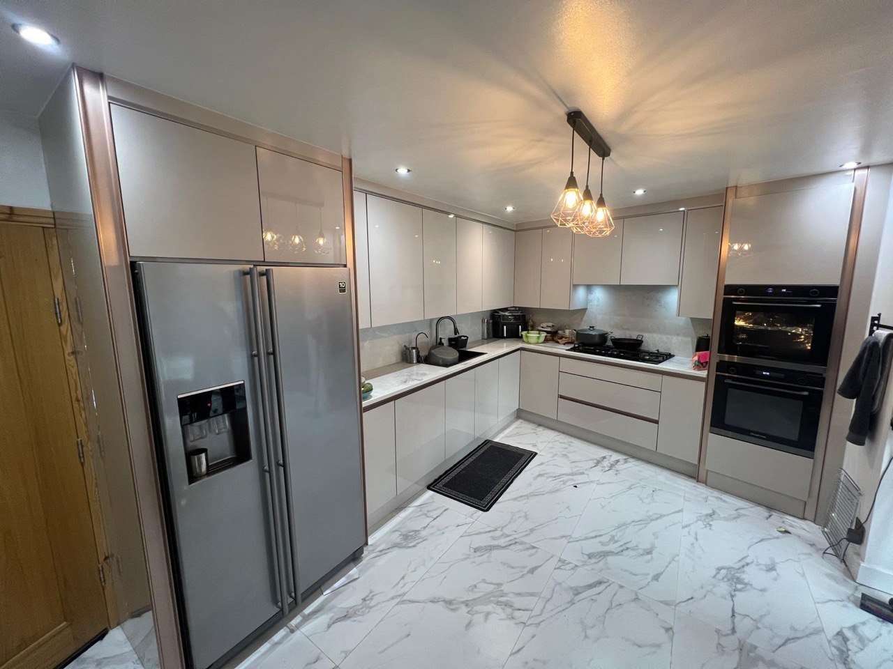 Completed MALCON handleless gloss kitchen in London with integrated ovens, pendant lighting and marble-effect floor tiles