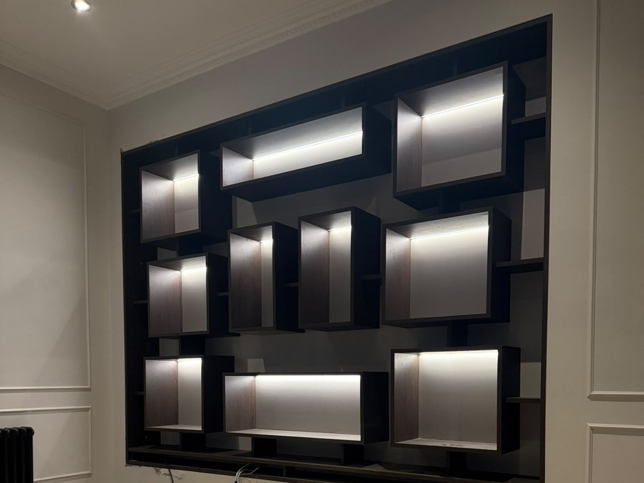 Black bespoke display wall by the MALCON team with staggered open boxes and integrated LED lighting, set into a panelled wall