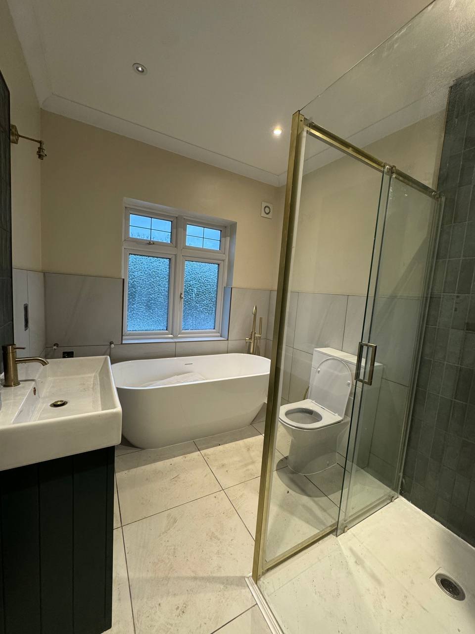 Bathroom with brass-framed walk-in shower, freestanding bath and vanity unit, renovated by MALCON