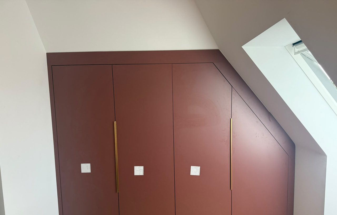 Fitted loft wardrobes by the MALCON team in a deep red finish with brass handles, cut to follow the sloping ceiling