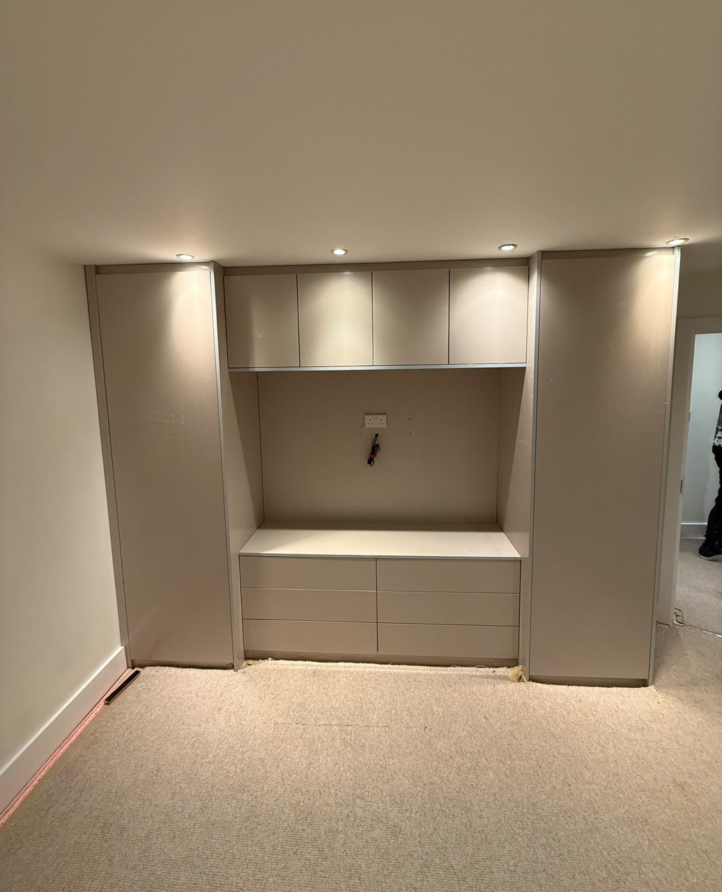 Fitted media and storage unit by the MALCON team in a taupe finish with a TV recess, drawers and concealed lighting