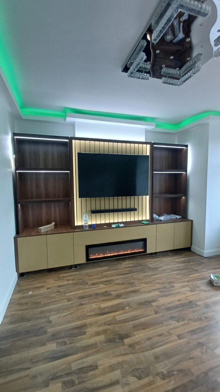 Completed MALCON fitted media wall in London with slatted centre panel, illuminated walnut-finish shelving and an inset electric fire