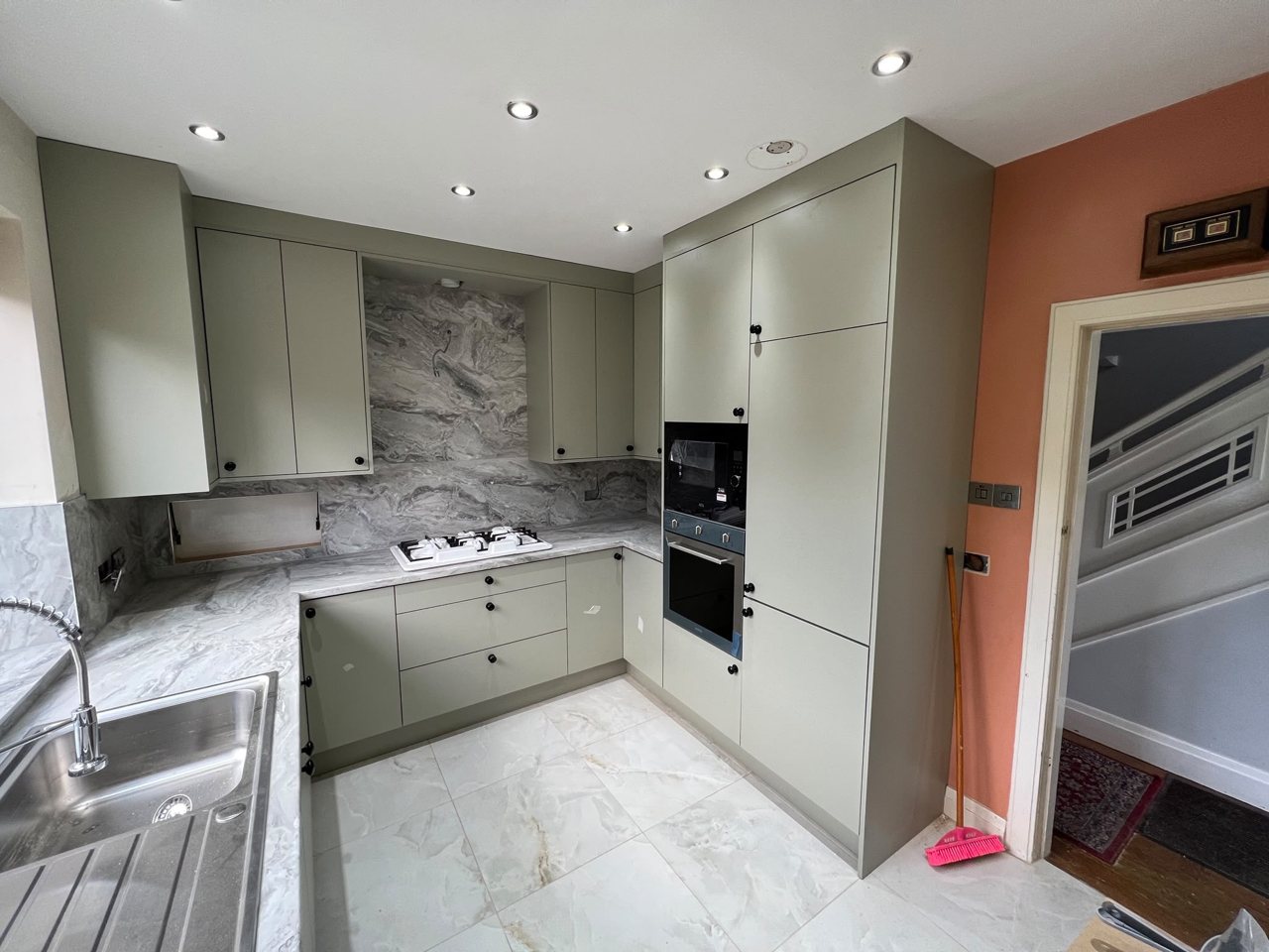 Sage green handleless kitchen by the MALCON team with a marble-effect splashback and worktop and integrated ovens